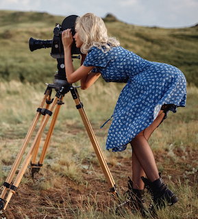 Woman using camera on tripod in open field