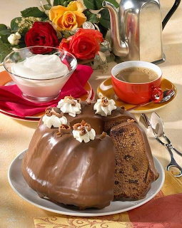 Chocolate bundt cake with glaze on white plate, teacup, roses, and decorative flowers on golden tablecloth