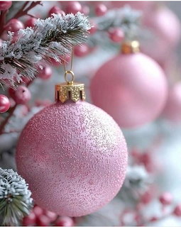 Frosted pink Christmas ornament hanging on snow-covered pine branch with blurred festive decorations in background
