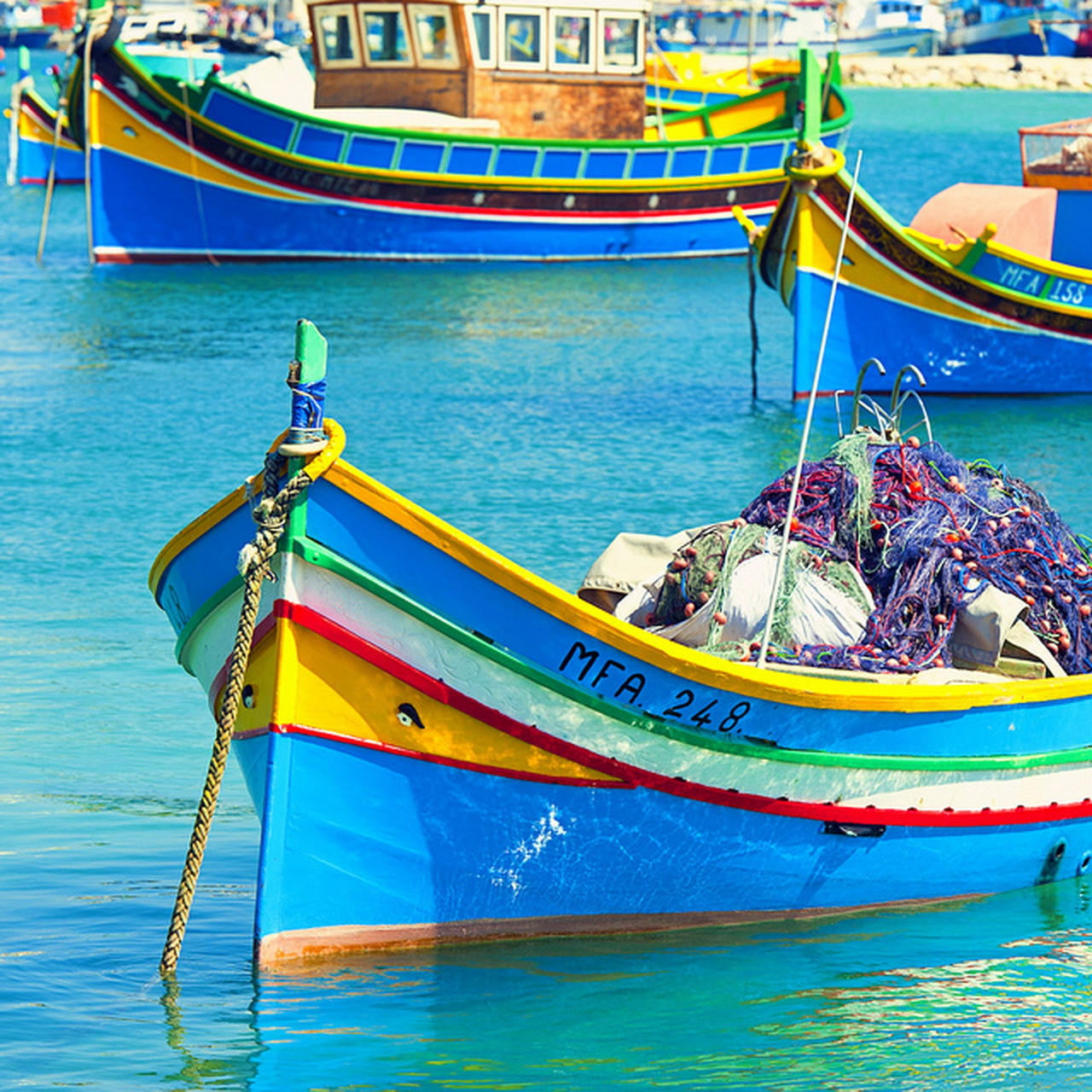 Brightly painted traditional Maltese fishing boats floating in clear turquoise harbor water