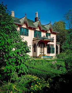 Pink Victorian cottage with ornate gables and green garden under blue sky