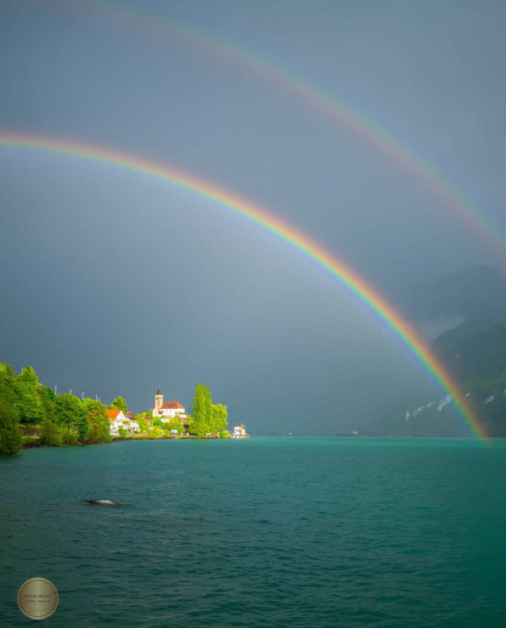 Double rainbow over a lake with a small village and green shoreline