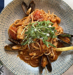 Seafood pasta dish with mussels, shrimp, and herbs in a textured ceramic bowl