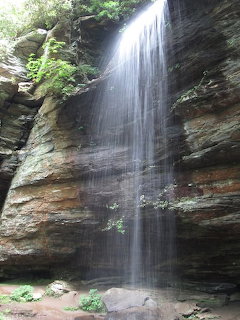 Tall waterfall streaming down a layered sandstone cliff with green plants at the top