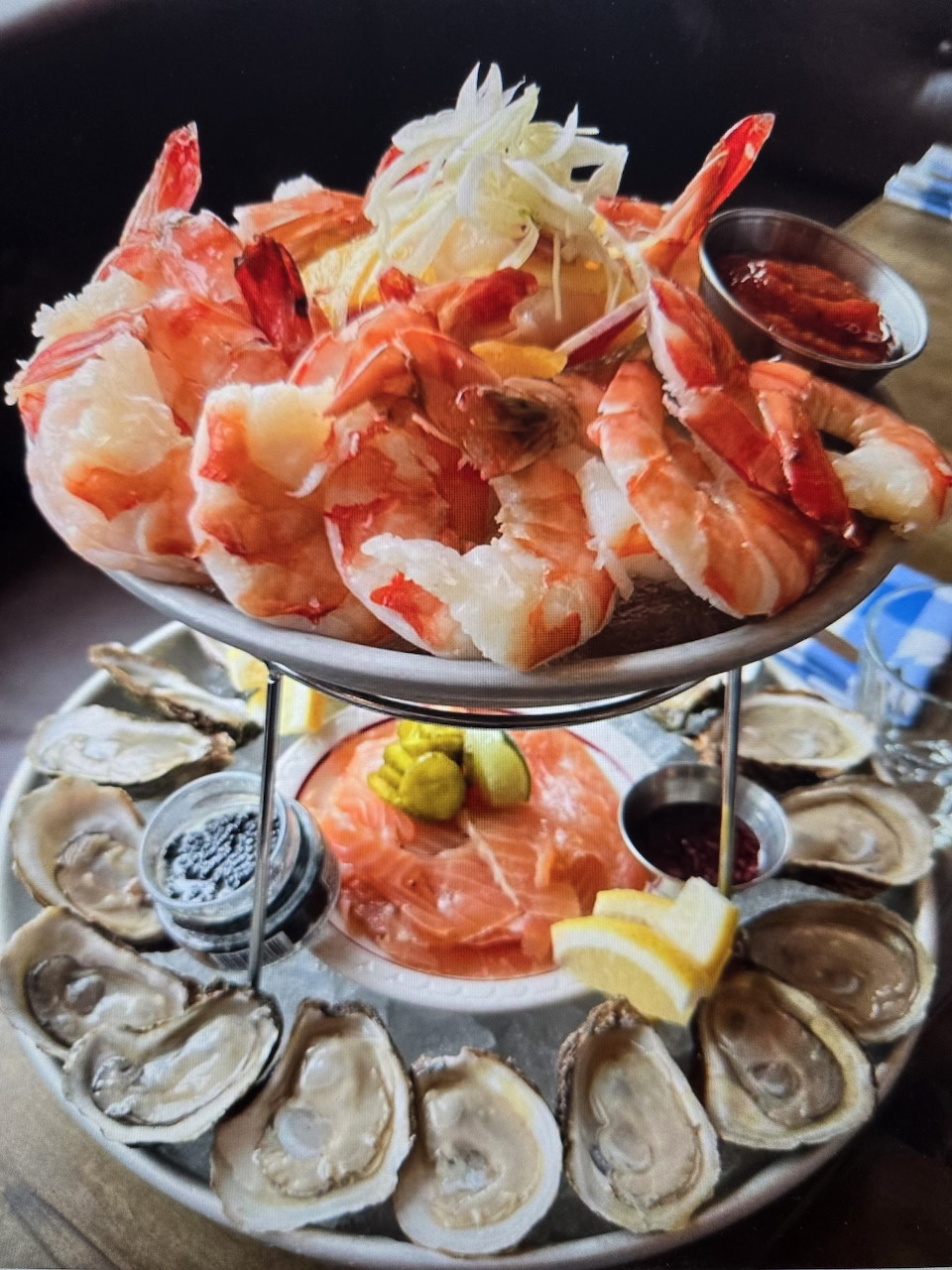 Tiered seafood platter with shrimp, oysters, smoked salmon, lemon, and dipping sauces