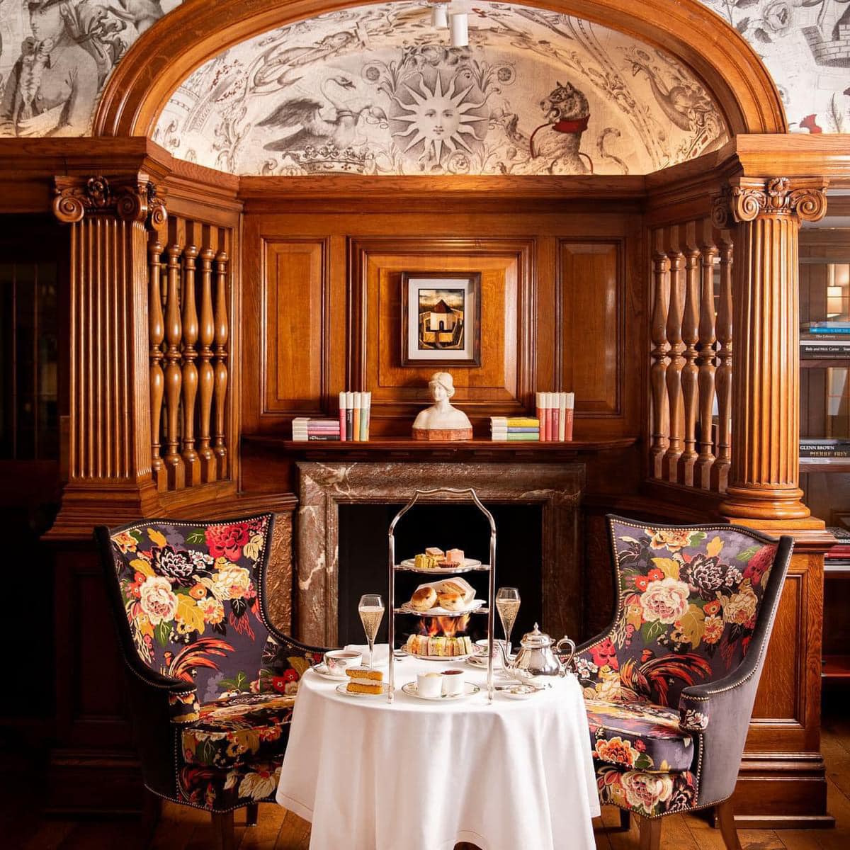 Afternoon tea table between floral armchairs in an ornate wood-paneled room