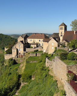 Historic French village with stone church and traditional buildings surrounded by green landscape