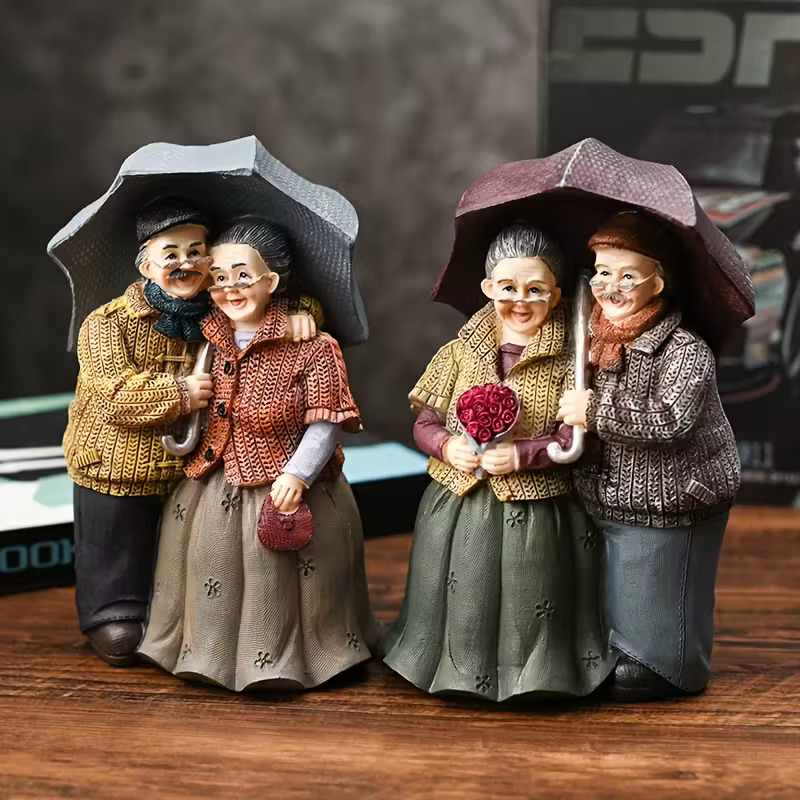 Two decorative figurines of elderly couples in vintage attire holding umbrellas and flowers