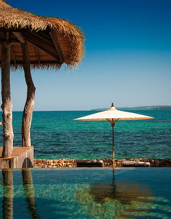 Thatched hut and white umbrella beside an infinity pool overlooking the blue ocean