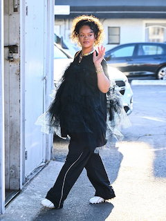 Rihanna in black tulle outfit and white slippers waving while walking on a sidewalk