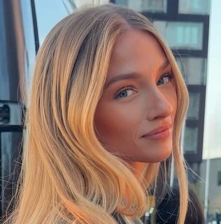 Close-up portrait of a blonde woman with wavy hair looking at the camera indoors