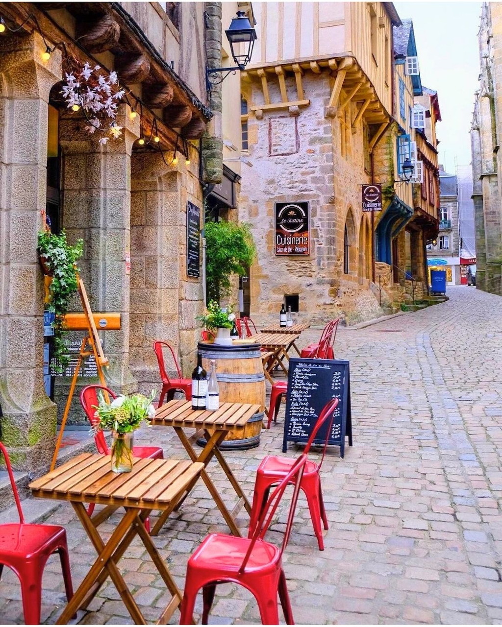 Outdoor cafe tables and colorful chairs on a European cobblestone street with stone buildings