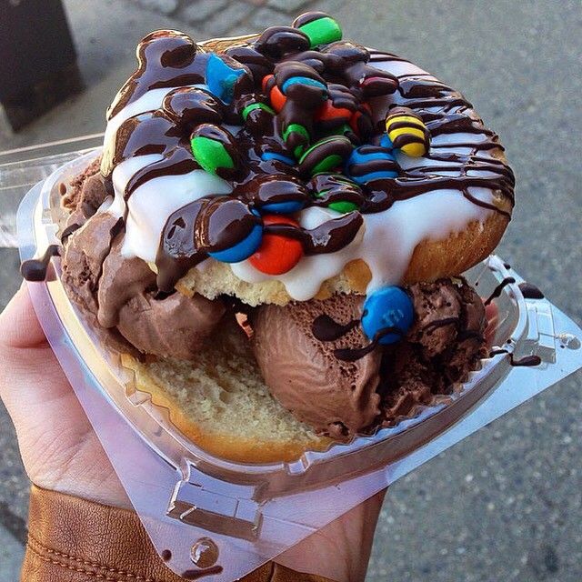 Hand holding a donut stuffed with chocolate ice cream and topped with icing, chocolate sauce, and candy