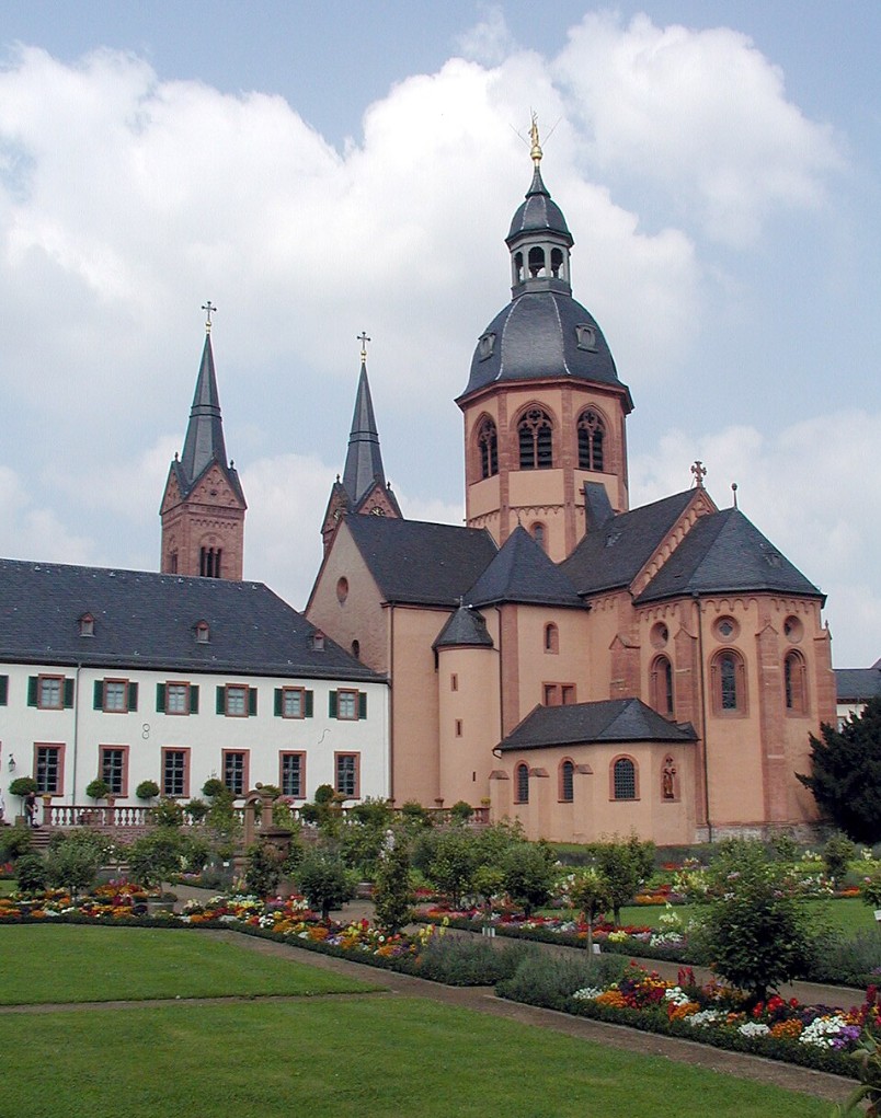 Historic basilica complex with towers and domes beside a flower garden and lawn