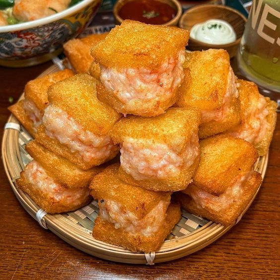 Basket of golden fried shrimp toast pieces with dipping sauces on a wooden table