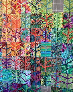 Colorful patchwork quilt with tree silhouettes in rainbow gradient from orange to green with mixed patterns