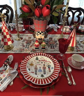Festive Christmas table setting with nutcracker, candles, red glasses, and holiday plates