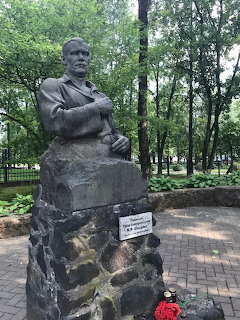 Stone statue on a pedestal beside a brick path in a wooded park