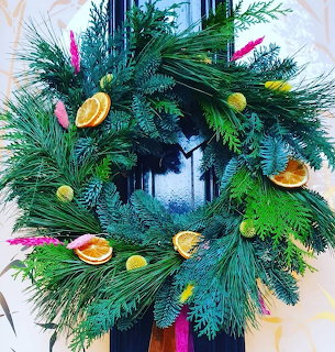 Green wreath with orange slices and colorful decorations hanging on a dark door