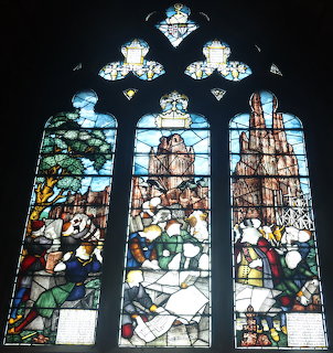 Stained glass window with three Gothic arched panels depicting medieval scenes in Lichfield Cathedral