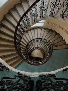 Spiral staircase with ornate iron railings viewed from above curving downward through multiple floors