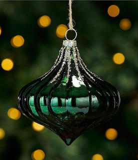 Dark green ribbed glass Christmas ornament hanging on a tree with bokeh lights in background