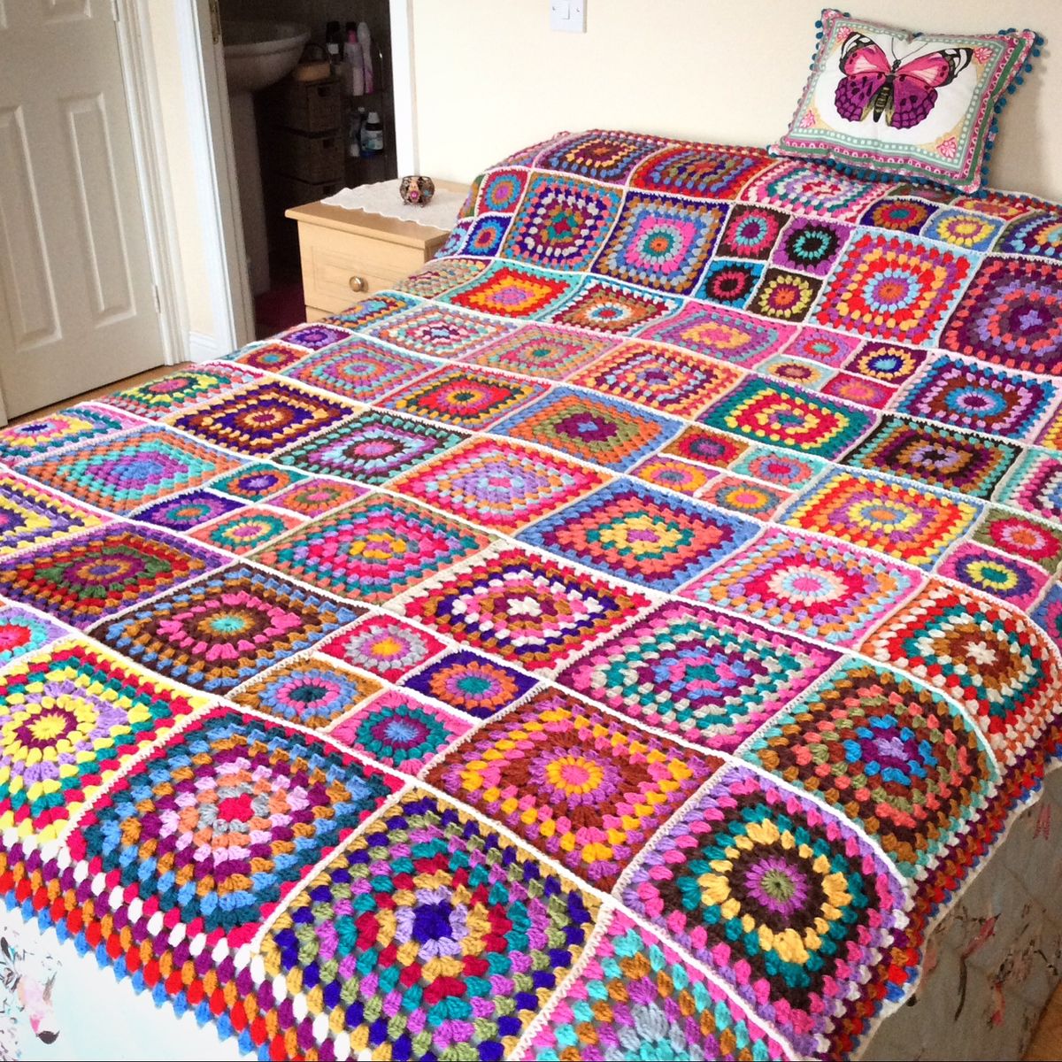 Bed with a colorful crochet granny square bedspread and butterfly pillow in a bedroom