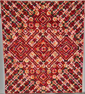 Geometric patchwork quilt with red, pink, and orange diamond patterns