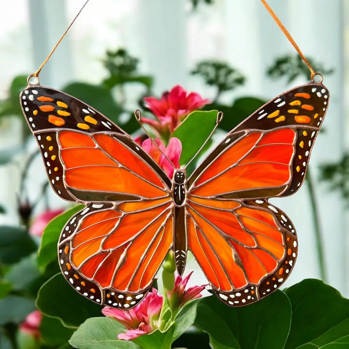 Orange butterfly suncatcher hanging above pink flowers and green leaves