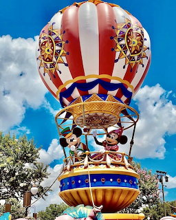 Colorful Disney carousel hot air balloon ride against blue sky with clouds