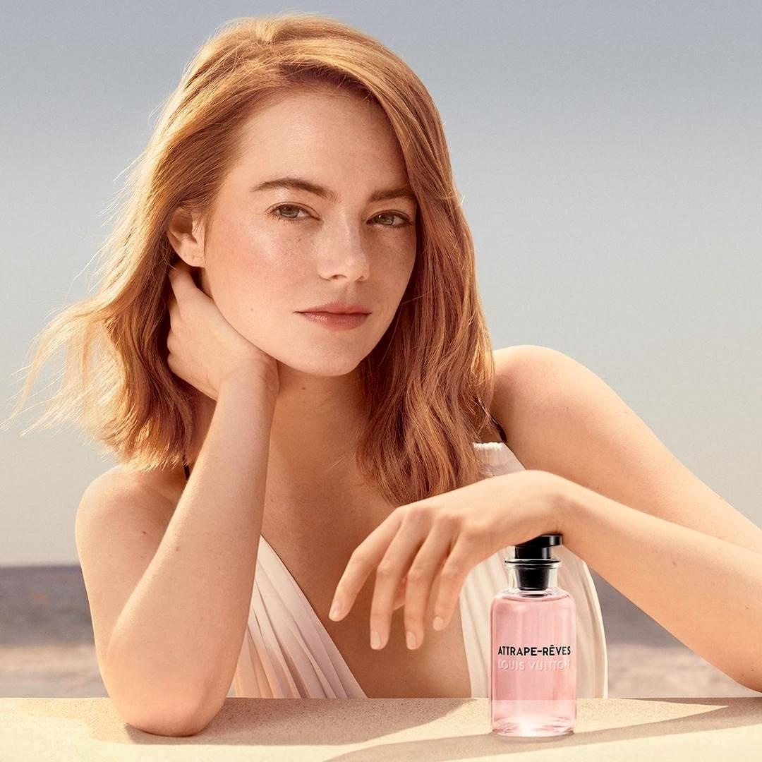 Emma Stone posing at a table beside the sea with a perfume bottle