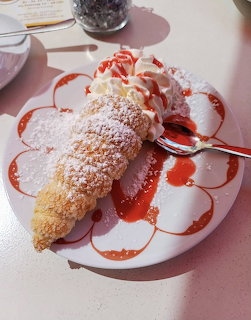 Cream-filled pastry roll with powdered sugar and strawberry sauce on white plate
