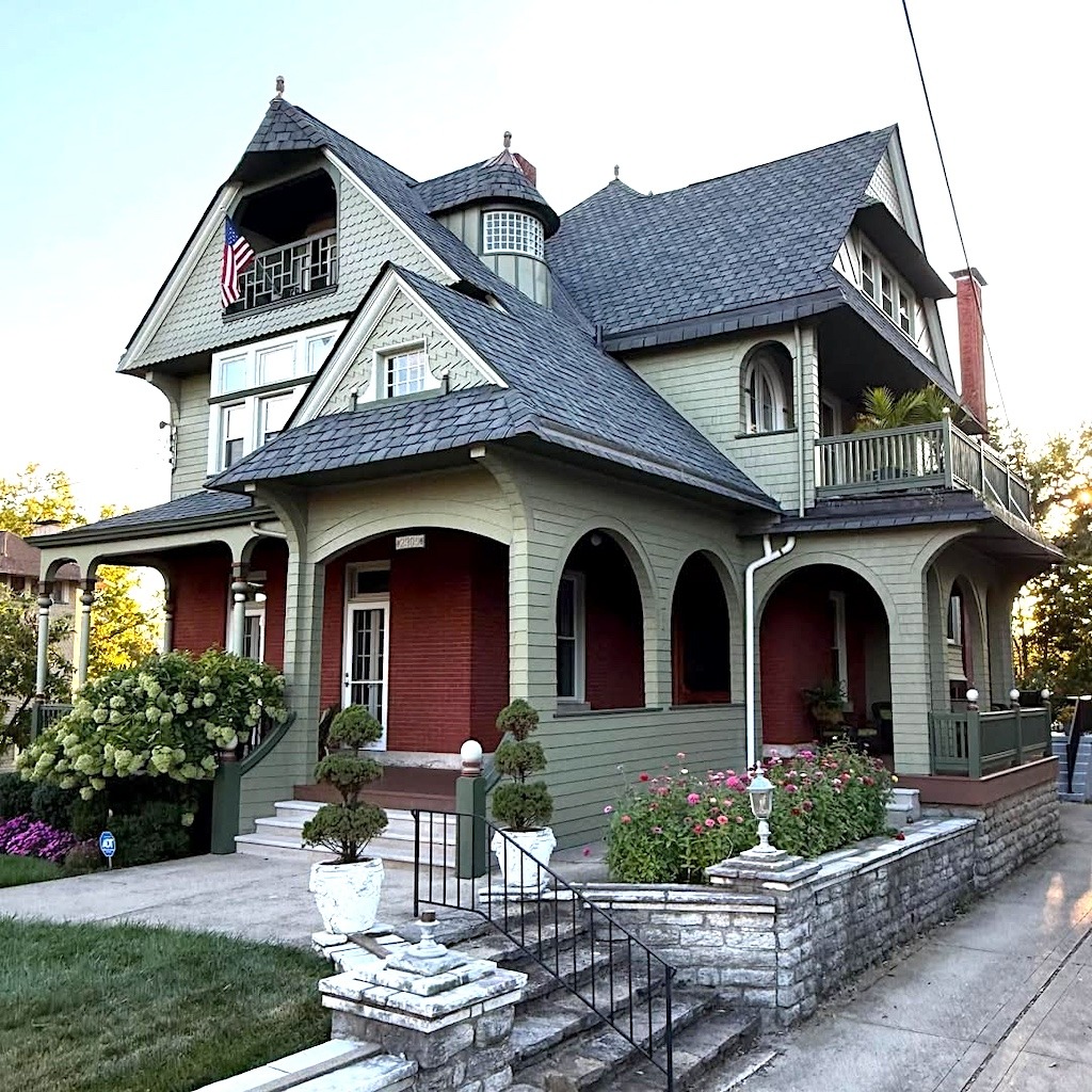 Victorian house with steep rooflines, arched porch, stone steps, and flowering garden in front