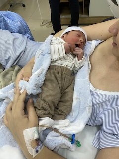 Newborn baby lying on a woman's chest in a hospital room with a blue blanket