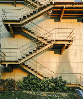 Metal zigzag exterior staircase on a beige building wall with green bushes below