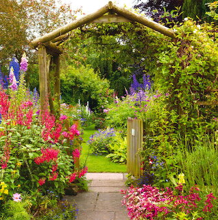Stone garden path under wooden arbor surrounded by colorful flowers and green foliage