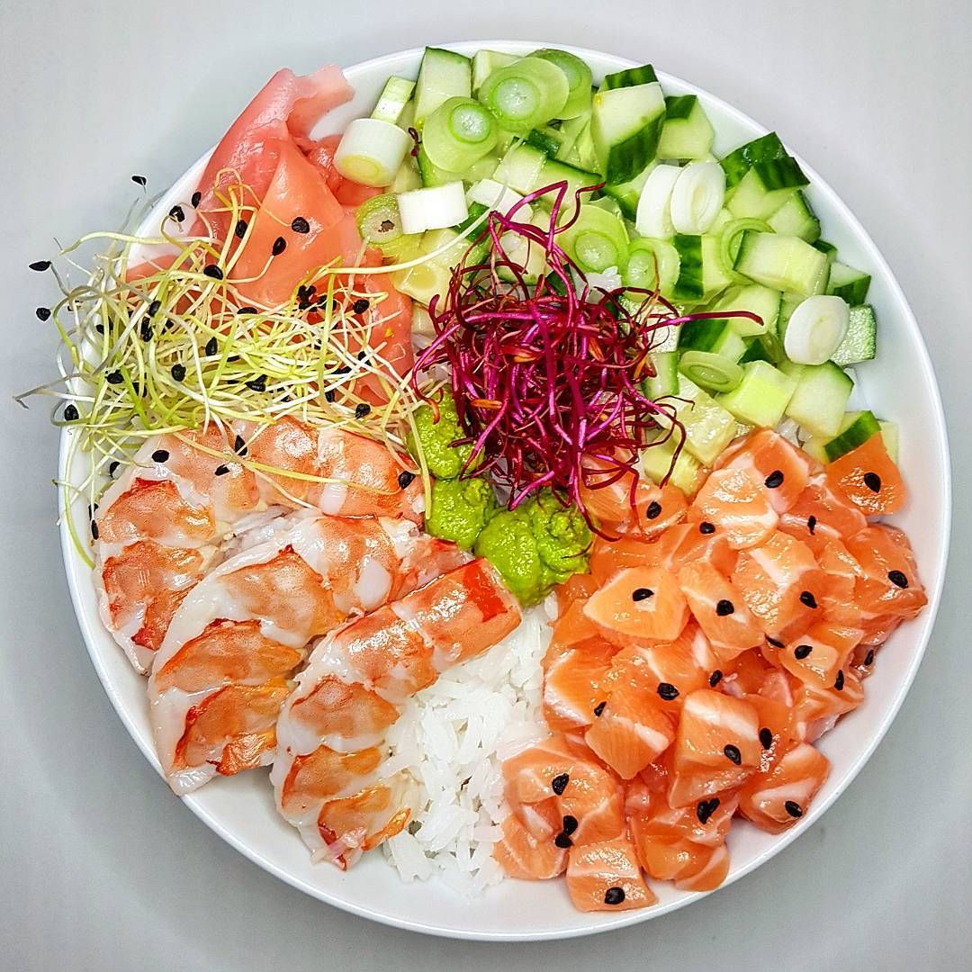 Overhead view of a sushi bowl with salmon, shrimp, cucumber, avocado, and vegetables on white rice