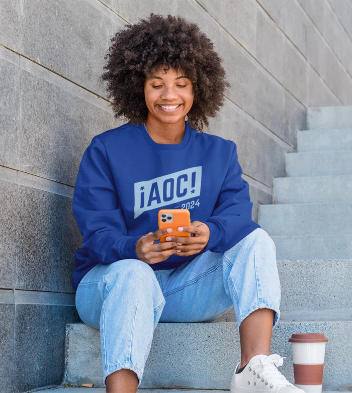Smiling woman in blue sweatshirt sitting on steps with phone and coffee