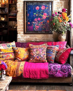 Bright pink sofa with multicolored decorative pillows and throws beneath blue floral artwork and flower vase