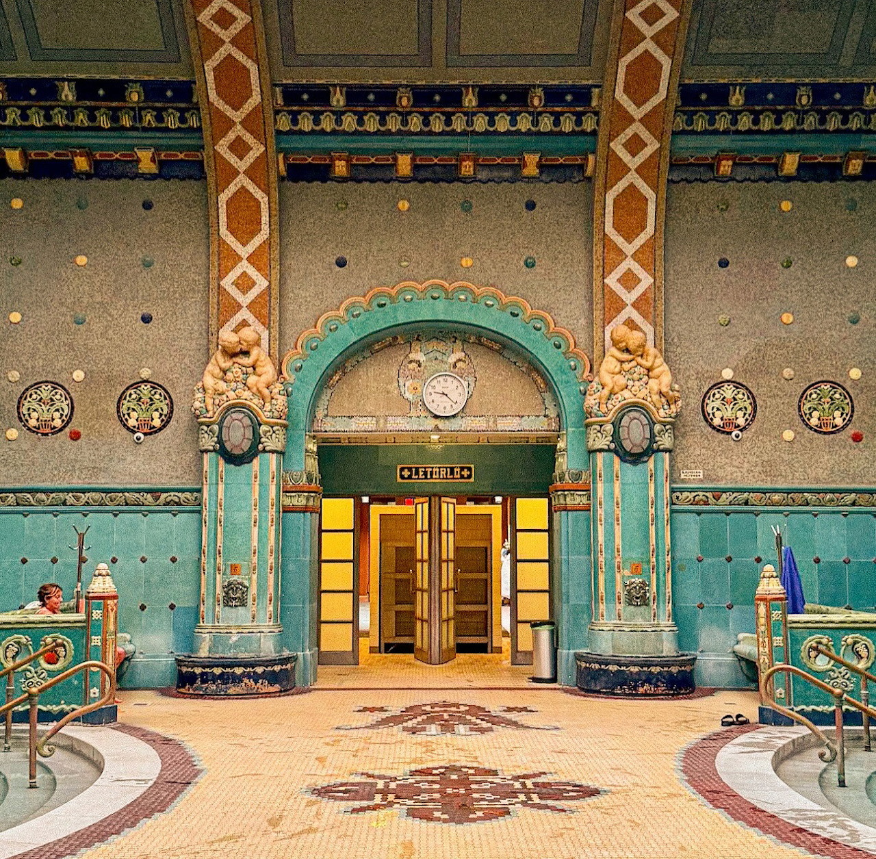Ornate tiled interior of Gellért Thermal Bath in Budapest with columns, doorway, and poolside railings
