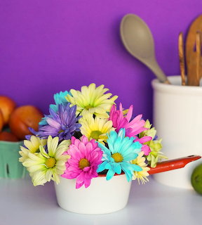 Bright multicolored daisies in white pot with kitchen utensils and purple wall