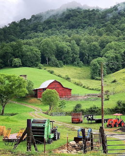 Red barn in green valley with tractors and forested mountains