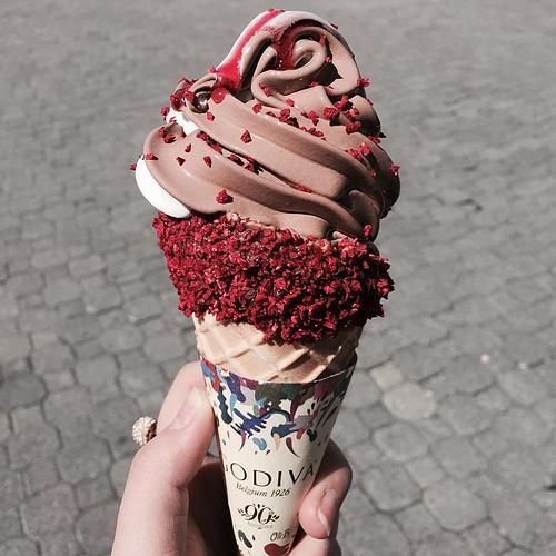 Hand holding Godiva chocolate gelato cone with pink frosting swirl and red velvet coating