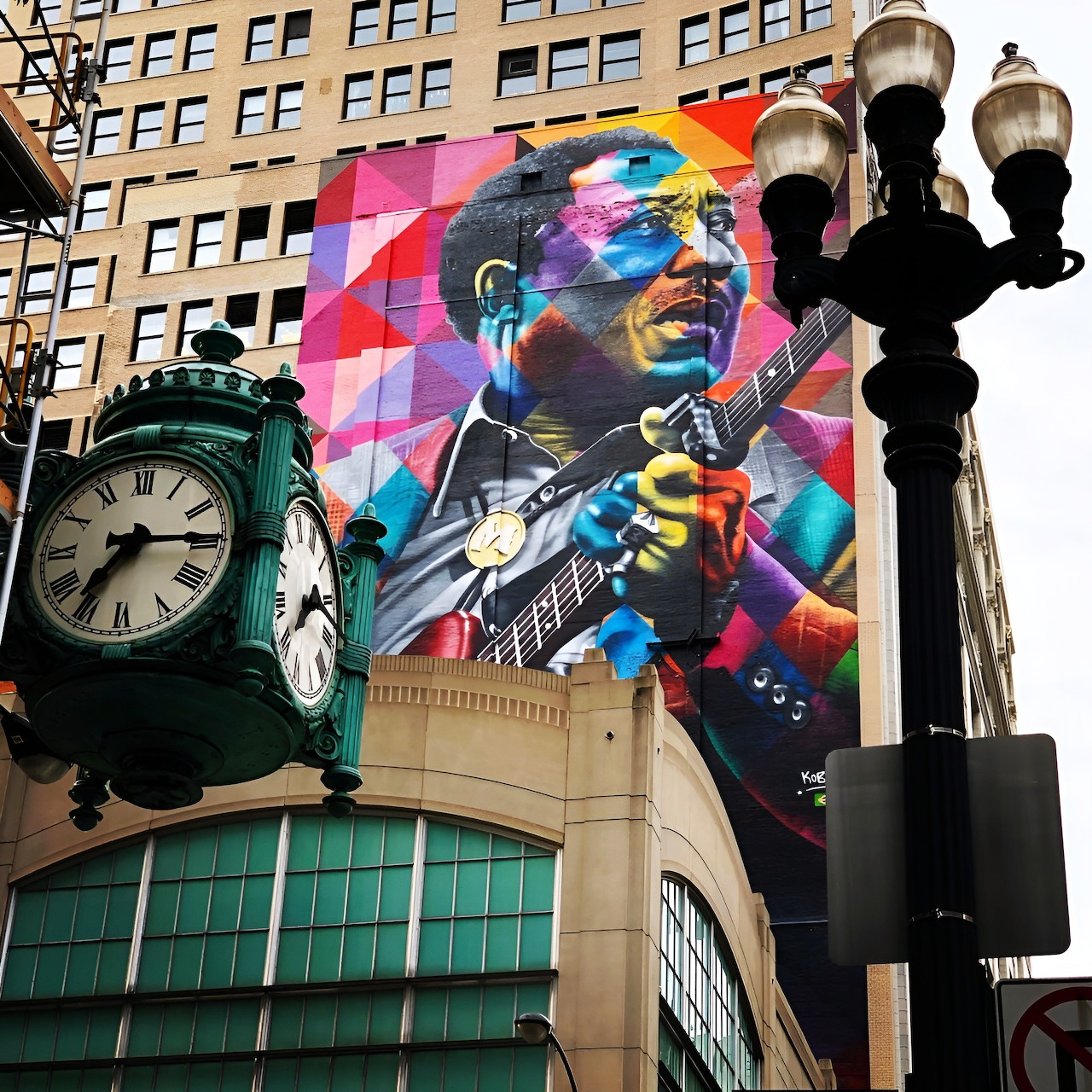 Colorful mural of Muddy Waters playing guitar on Chicago building with ornate street clock in foreground