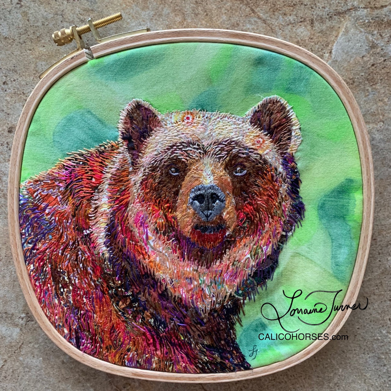 Colorful embroidered bear portrait in a hoop with a green background