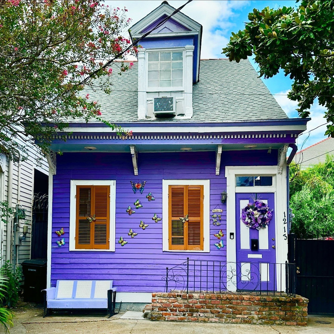 Purple house exterior with butterfly wall decorations, brown shutters, and a wreath on the front door