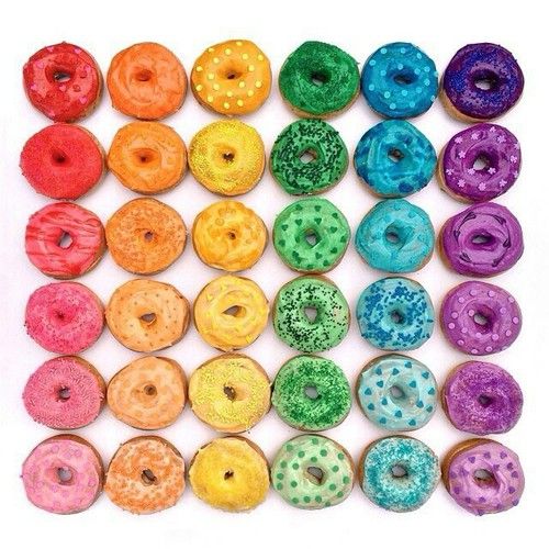 Grid of 36 colorful glazed donuts in rainbow colors with various sprinkle toppings arranged in neat rows