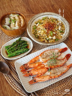 Overhead view of Asian meal with grilled shrimp, fried rice, asparagus, and soup on woven mat