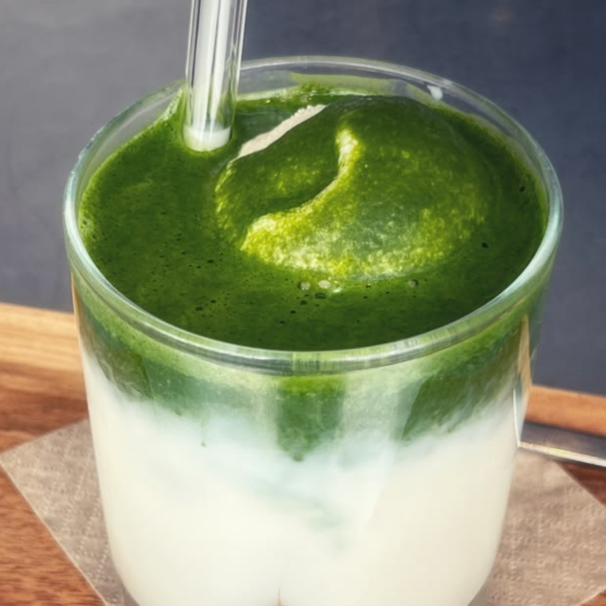 Glass of iced matcha latte with green foam over milk on a wooden table