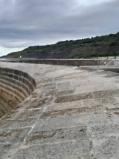 Curved stone harbour wall of The Cobb at Lyme Regis with steps and overcast sky